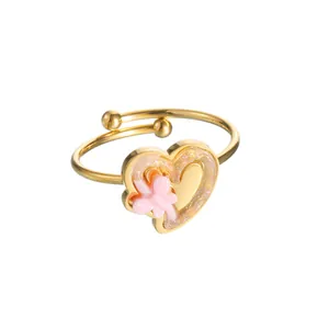 Detail of a golden heart ring with pink flower inlay and glitter finish on a white background