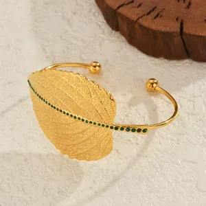 Goldenes Blatt-Armband mit grünen Strasssteinen auf strukturiertem weißem Stein