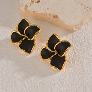 Minimalist flower stud earrings in black and gold with textured petals on stone background
