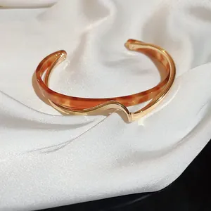 Détail d'un bracelet manchette doré ondulé avec résine ambre sur tissu de soie blanche