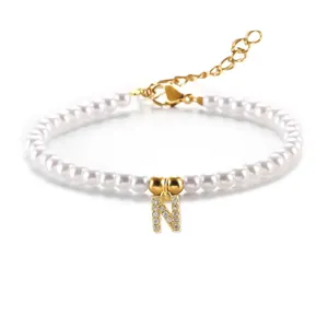 Detail van witte parelarmband met gouden letter N-hanger en glinsterende zirkonen