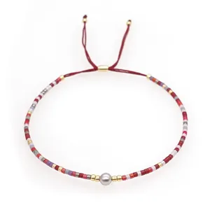 Detail of bohemian red braided bracelet with colorful beads and a central grey pearl