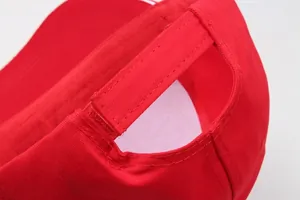 Macro detail of red cotton baseball cap showing adjustable velcro strap and twill texture