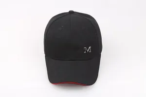 Dettaglio del cappello in cotone con logo M in metallo argento e bordo rosso sottile
