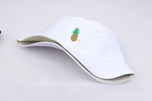 Detalle de gorro de pescador blanco con bordado de piña amarilla y texto Pin