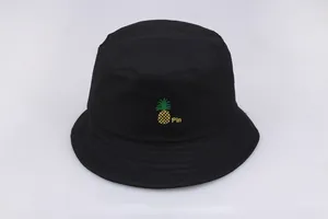Detalle de gorro de pescador negro con bordado de piña amarilla y el texto Pin