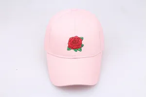 Detail shot of a light pink baseball cap featuring red rose embroidery and cotton texture