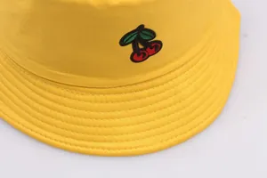 Close-up of yellow cotton bucket hat featuring detailed red cherry embroidery on the crown