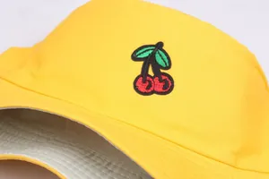 Detail of yellow cotton bucket hat featuring embroidered red cherries and green leaves
