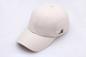 Détail de la casquette beige avec broderie noire de la lettre M sur le côté