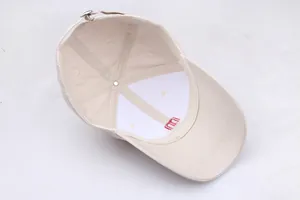 Detail van de binnenkant van een beige katoenen pet met rode m-borduring en metalen gesp