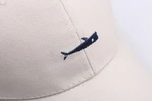 Detailed view of dark blue whale embroidery on beige cotton twill baseball cap