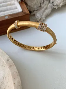 Detalle de brazalete dorado cepillado con pedrería brillante y diseño interior calado fino