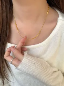 Detail of a cascading gold necklace on a white knit sweater with a pavé diamond ring
