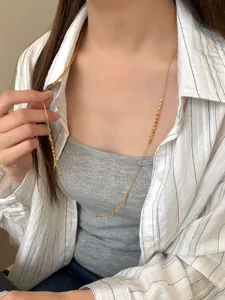 Detail view of a long gold S925 sterling silver chain necklace on a model wearing white
