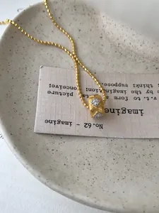 Detail van een gouden cilindervormige hanger met vierkante zirkoon en geborstelde afwerking