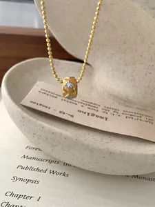Detail van matgouden cilinder hanger met diamantpatronen aan een fijne kralenketting