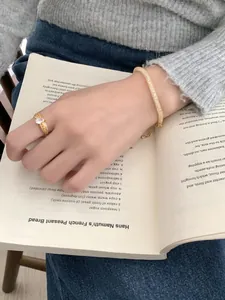 Detail of elegant gold bracelet with pavé stones and a woven ring on a lifestyle background