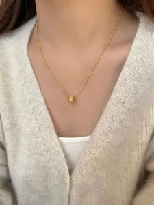 Detail van gouden S925 ketting met cilindervormige hanger op een beige gebreide trui