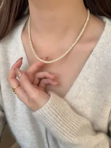 Gros plan du collier sac d'argent doré serti de pavés porté sur un pull en maille blanc