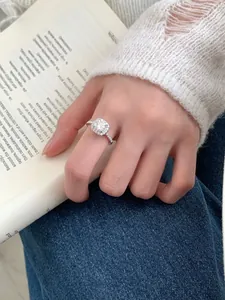 Detail of a square cut moissanite ring showing halo setting on a model's hand