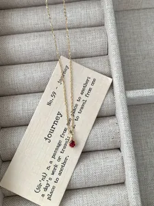 Close-up of gold chain with red teardrop pendant on minimalist card in jewelry tray