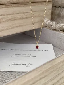 Detail of S925 silver gold-plated necklace with red zircon pendant over gift box