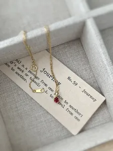 Detail of a gold water-drop necklace with a red gemstone on a soft jewelry box