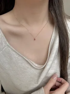 Close-up of elegant rose gold necklace with a red teardrop pendant on a model neck