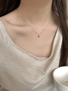 Close-up of a minimalist S925 silver necklace with a red teardrop pendant on the collarbone