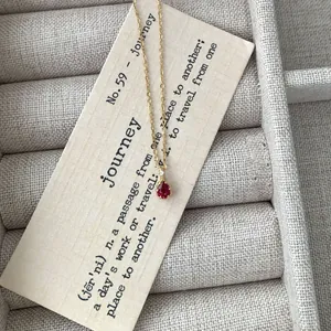 Elegant gold S925 silver necklace with red teardrop pendant on a beige jewelry box