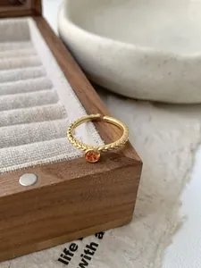 Détail d'une bague torsadée dorée ornée d'une pierre précieuse ronde de couleur orange