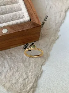 Détail de la bague torsadée dorée ornée d'une pierre précieuse de couleur verte