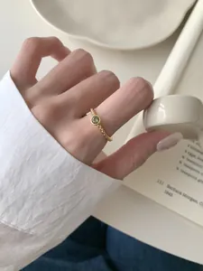 Détail d'une bague torsadée dorée ornée d'une pierre précieuse verte portée au doigt