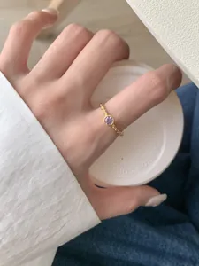 Détail d'une bague tressée dorée avec une pierre précieuse violette au doigt