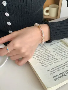Dettaglio del bracciale di perle rosa e anello in argento con pietra blu sulla mano