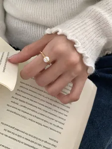 Detalle de un anillo giratorio de oro con circón en el dedo con fondo de libro y suéter suave