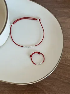 Dettaglio del set di gioielli con filo rosso e ciondoli in argento su piatto beige
