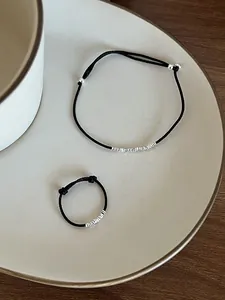 Dettaglio del set bracciale e anello in corda nera con accenti argentati su ceramica