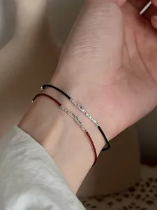 Dettaglio di braccialetti in corda intrecciata rossa e nera con perle in argento S925 al polso