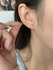 Primer plano de pendientes triangulares minimalistas de plata S925 en la oreja del modelo