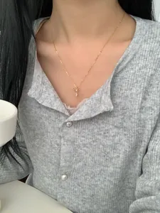Close-up of a gold bow and teardrop zircon pendant necklace on a model wearing knitwear