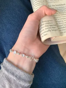 Détail d'un bracelet en argent S925 avec fleurs de pêcher porté au poignet avec un livre