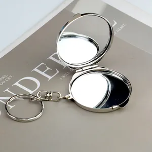 Portable mini round silver metal folding double-sided makeup mirror keychain on magazine background