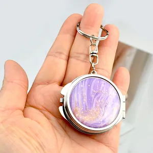 Detail of a mini round metal mirror keychain with purple marble and gold glitter design