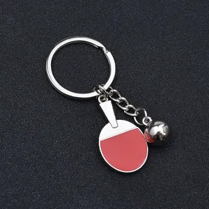 Table tennis paddle keychain with silver ball and red metallic finish on black surface