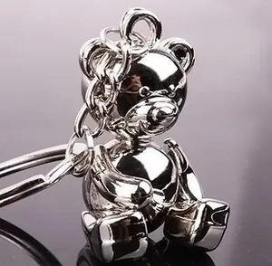 Polished silver metal teddy bear keychain with glossy finish on reflective dark surface