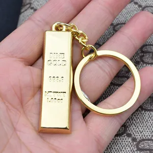 Polished gold bar keychain with 999.9 engraving held by hand over fabric background