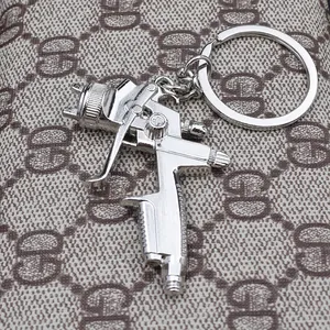 Creative silver spray gun keychain made of polished metal on a patterned background