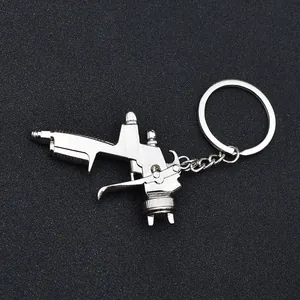 Polished silver metal spray gun keychain accessory on dark textured background